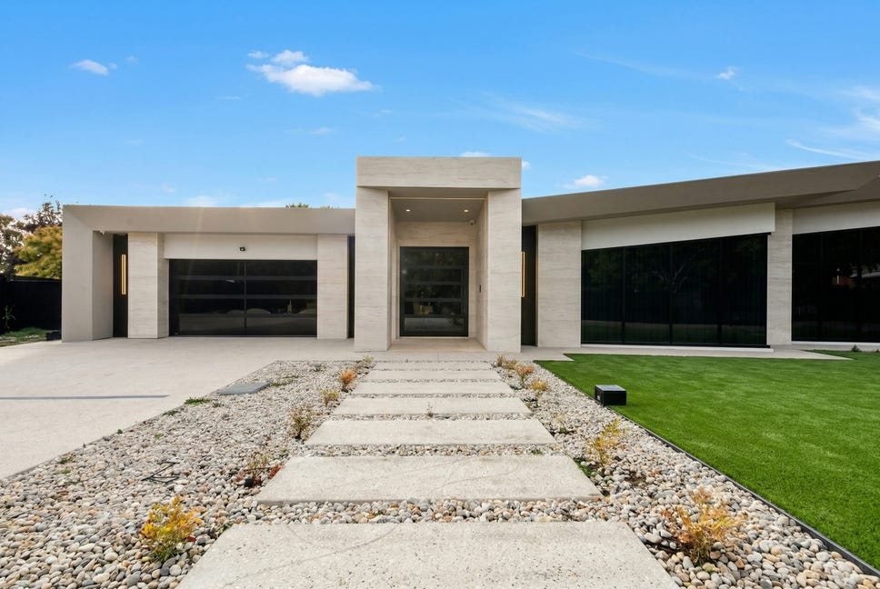Single-storey home with a stone-clad entry portal and black-framed glazing, reached by a stepping-stone path through a pebble garden