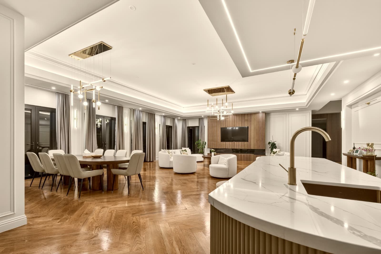 Open-plan living and dining with herringbone timber floors, a marble-topped island with brass tapware and linear brass pendant lights